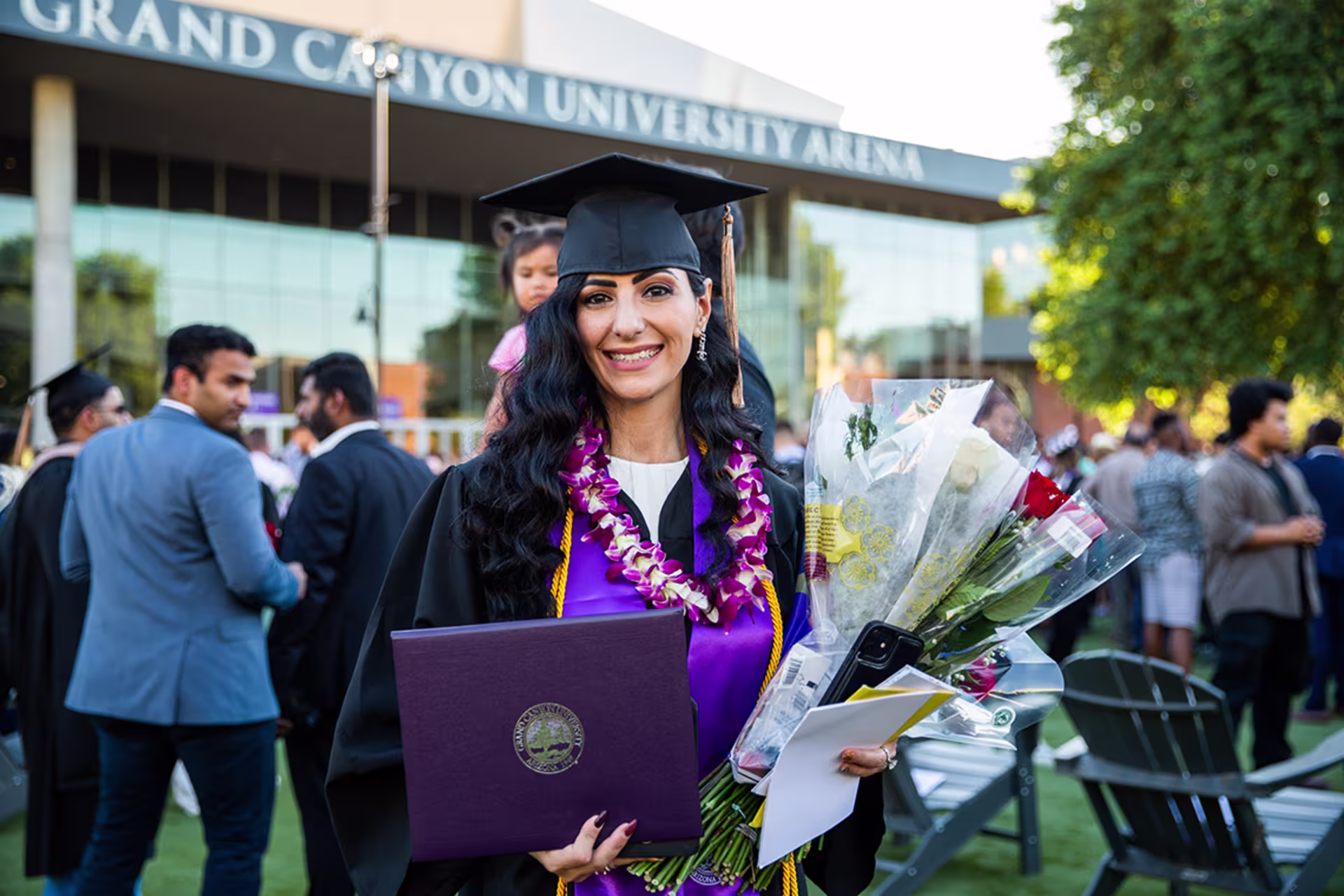 Female business bachelor’s graduate in cap and gown, and holding degree and flowers for camera