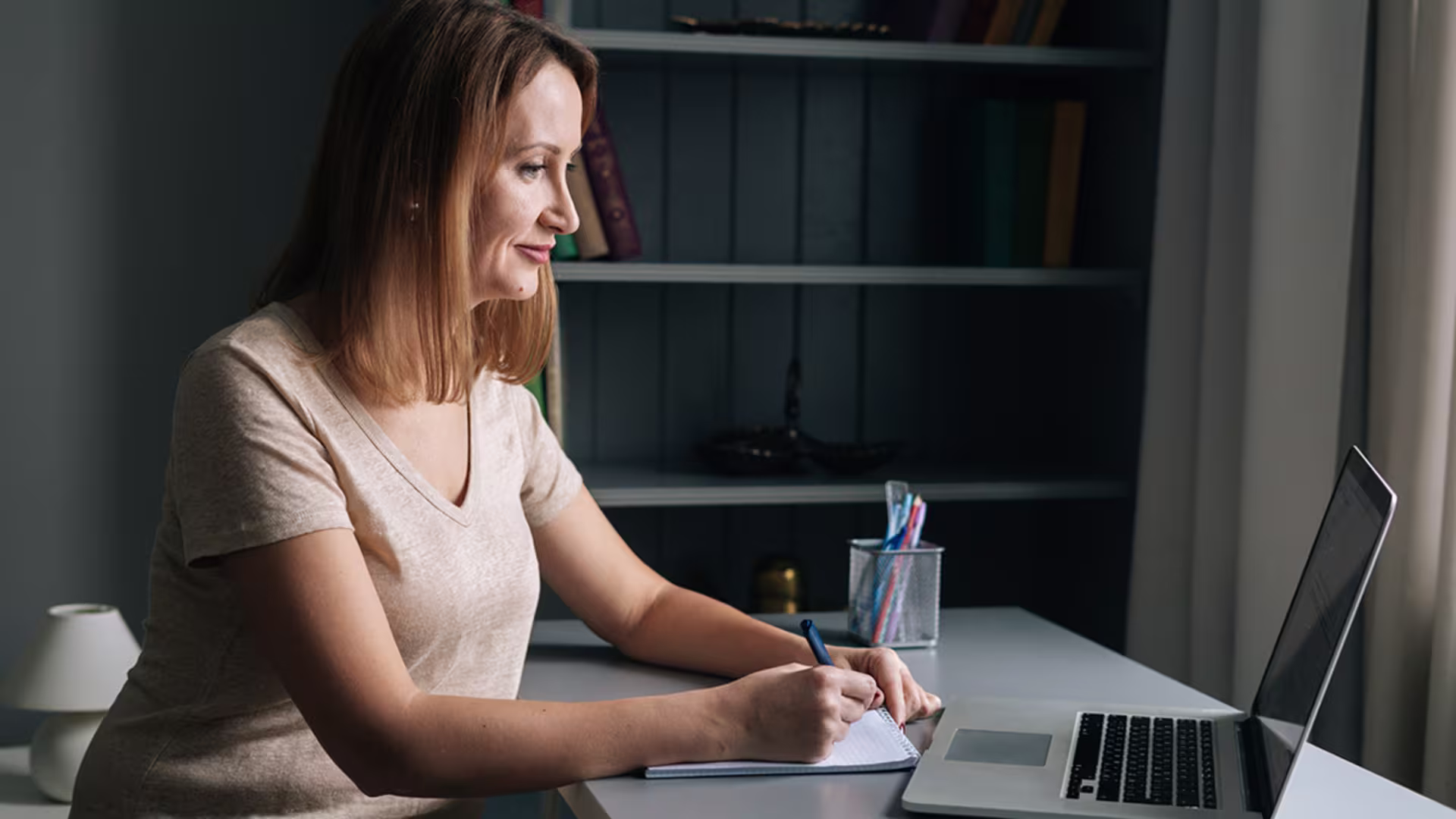 middle aged brunette woman in tan vneck handwrites paper outline
