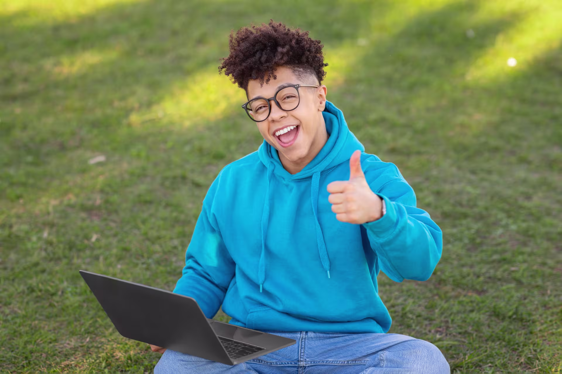 student with a computer sitting outside giving thumbs up