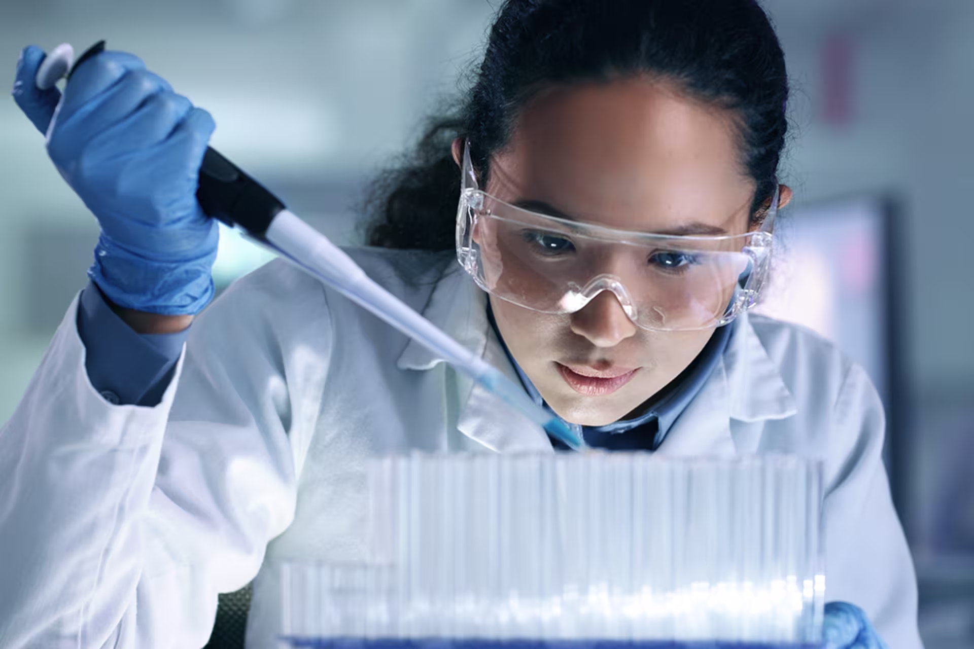 Asian female forensic scientist uses long pipette to put solution into test tubes with evidence in them