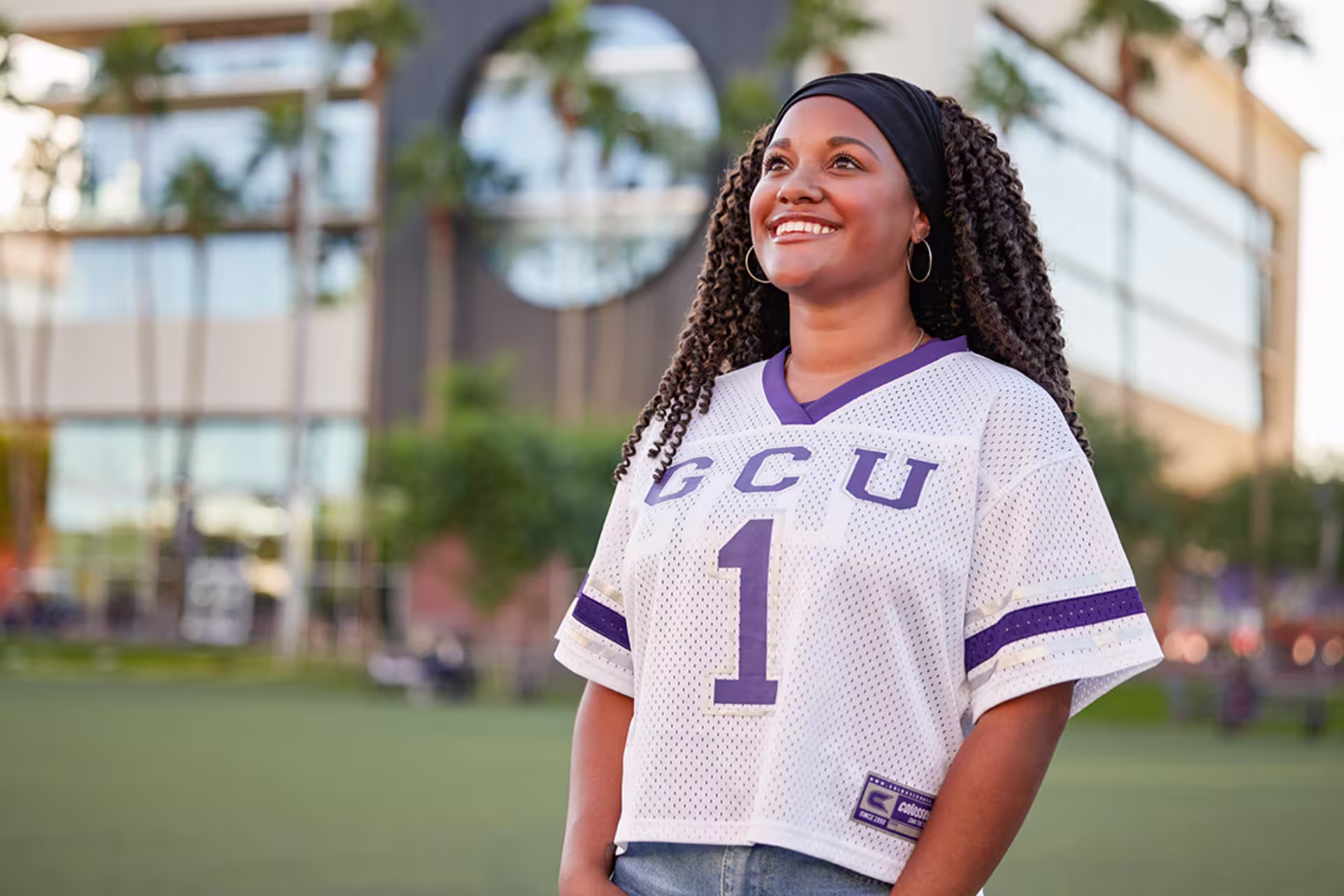 Female student outside wearing jersey and looking up at the sky