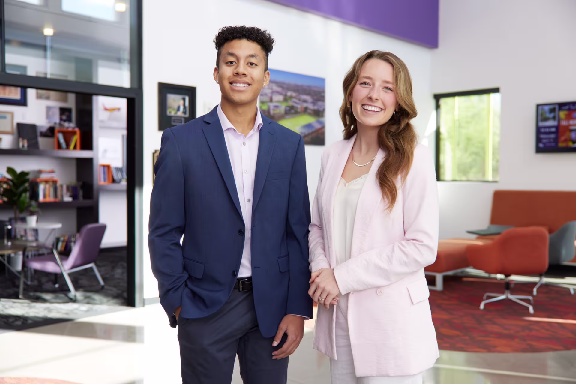 Male and female business majors smiling while wearing suits in office building