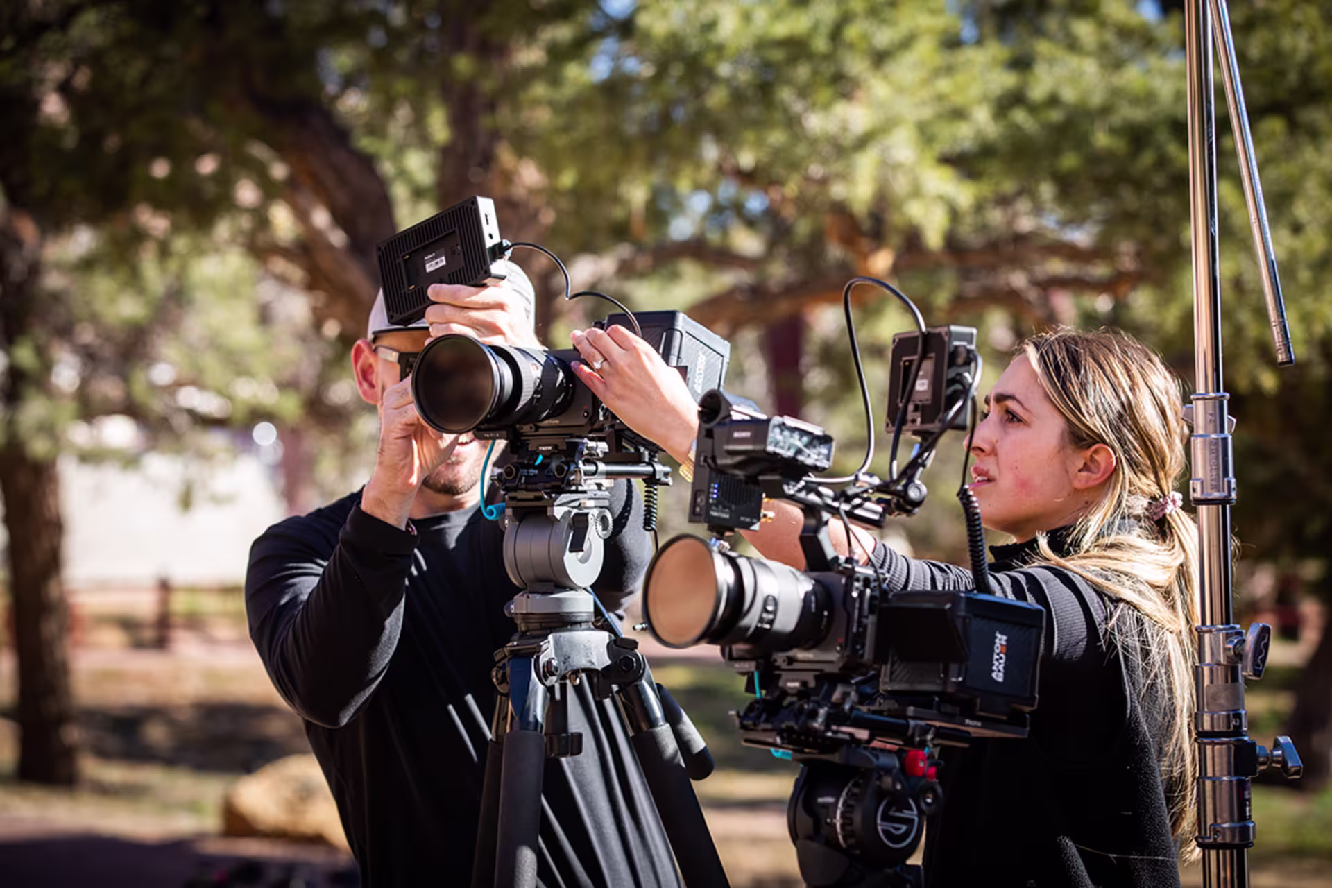 Male and female students adjusting video cameras for outdoor shoot