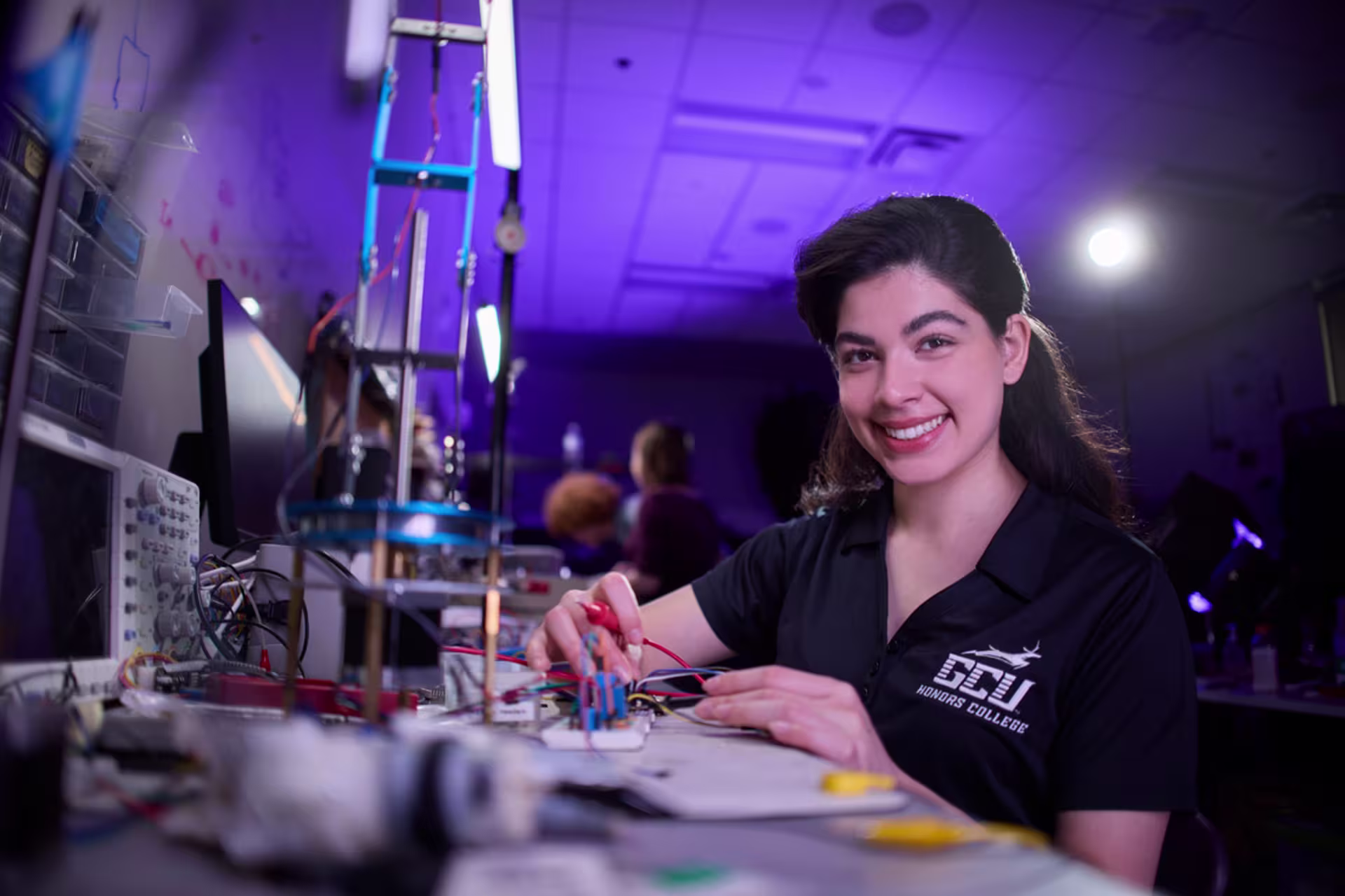 Student in GCU mechanical engineering technology mechatronics lab with electronic equipment and ambient lighting.