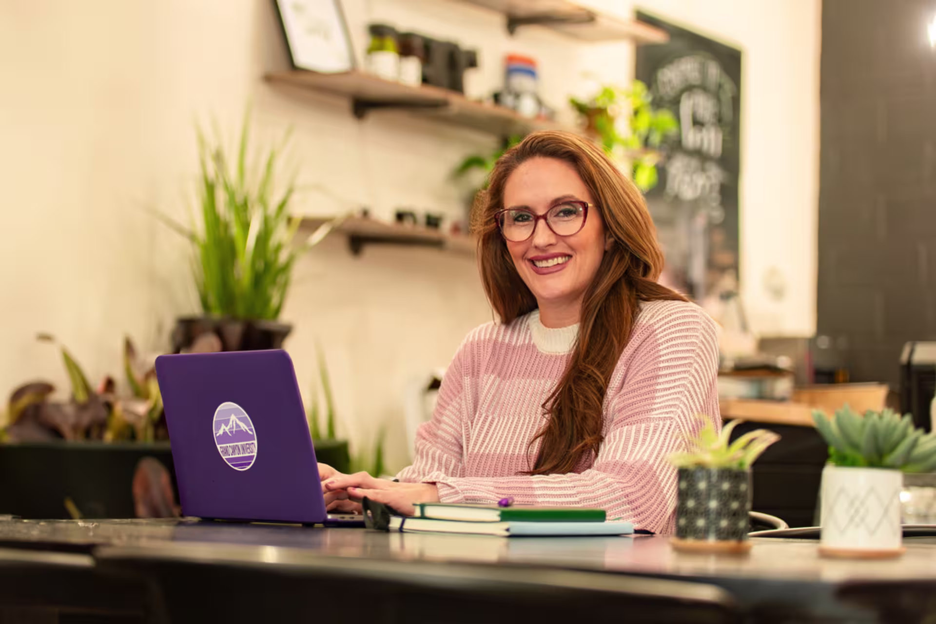 Christian leadership student working on a purple laptop in a coffee shop setting.