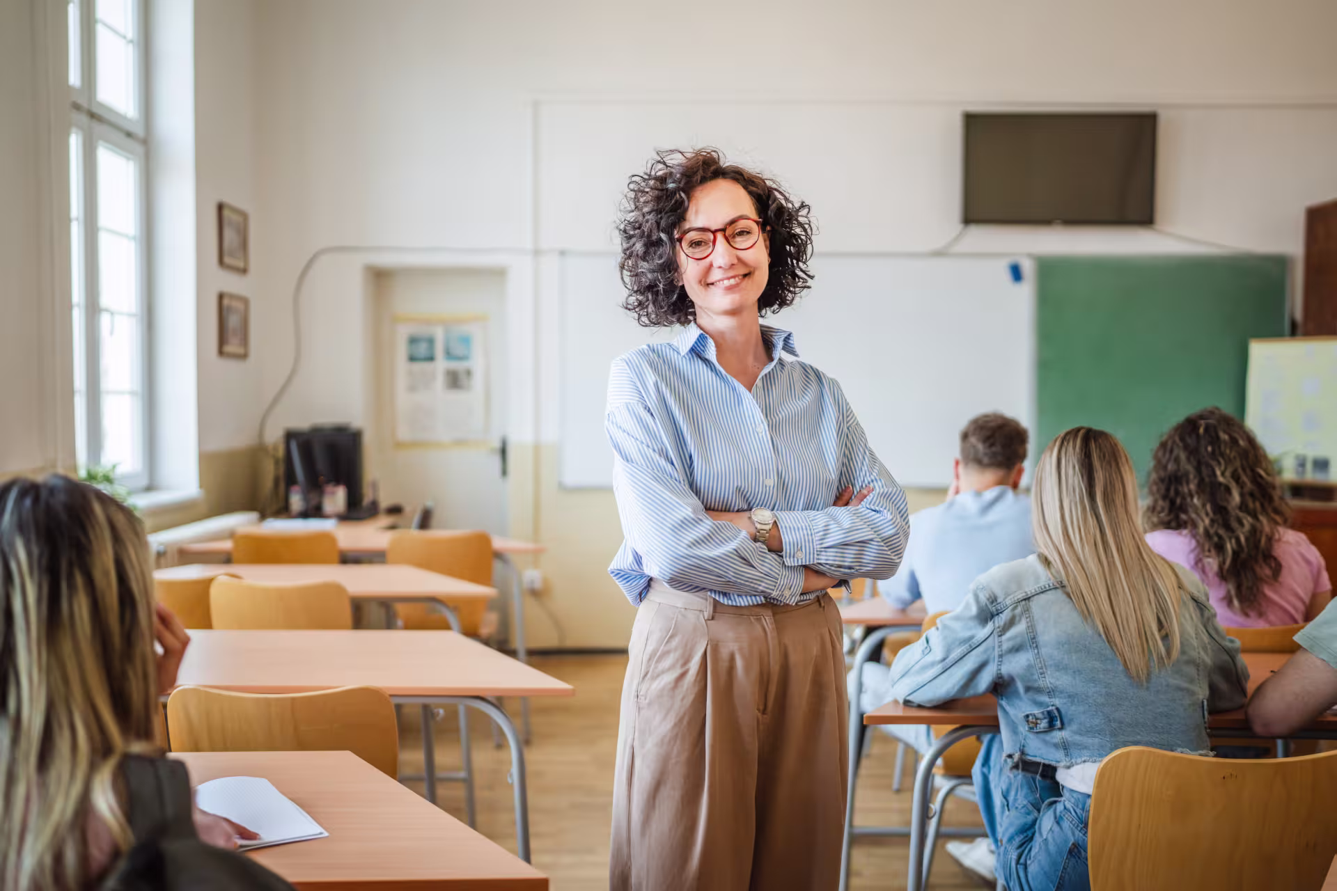 Education professional standing near desks with forward-facing students.