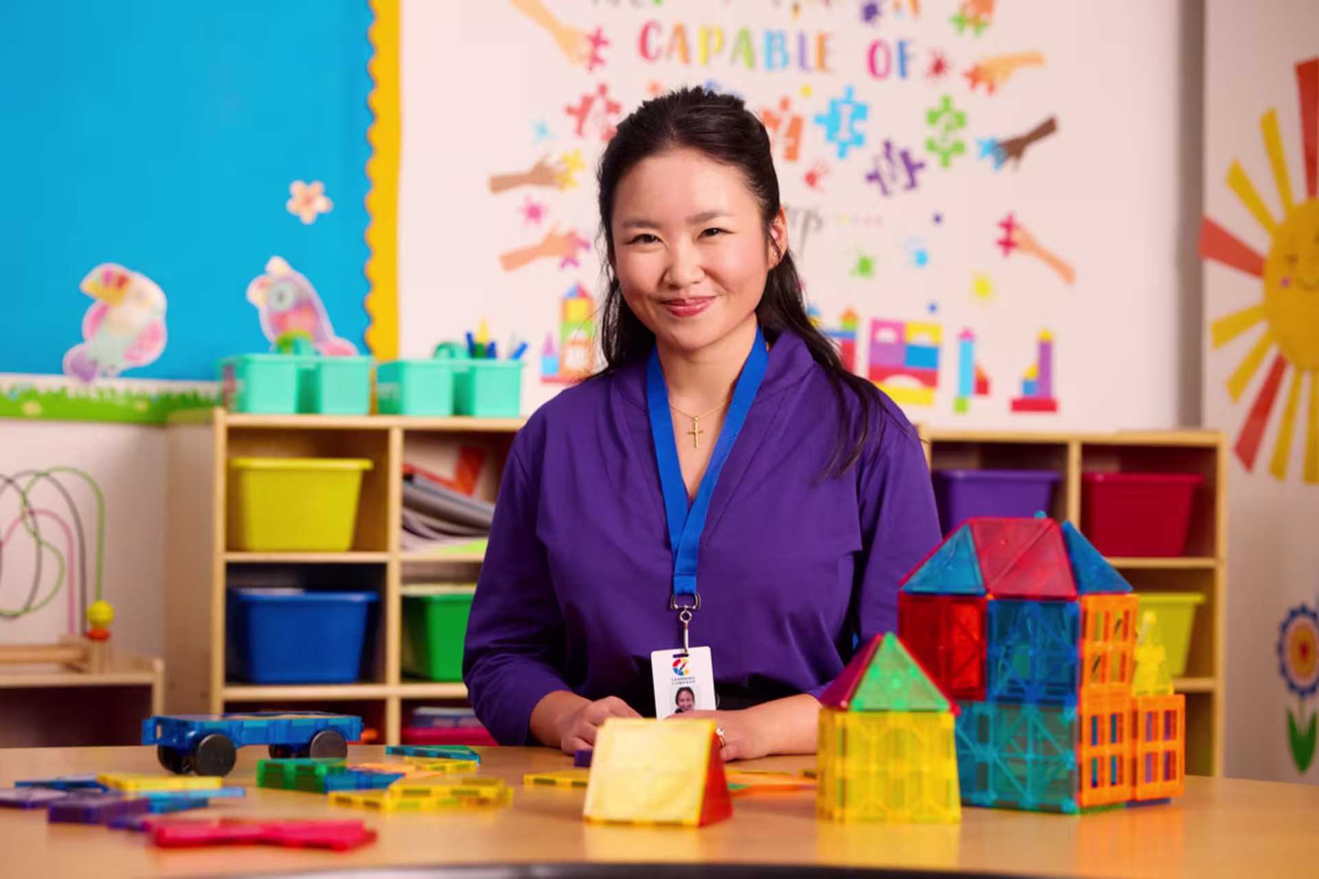 A female MEd in Special Education student smiles while sitting at a table in a classroom with children’s building toys on it. 