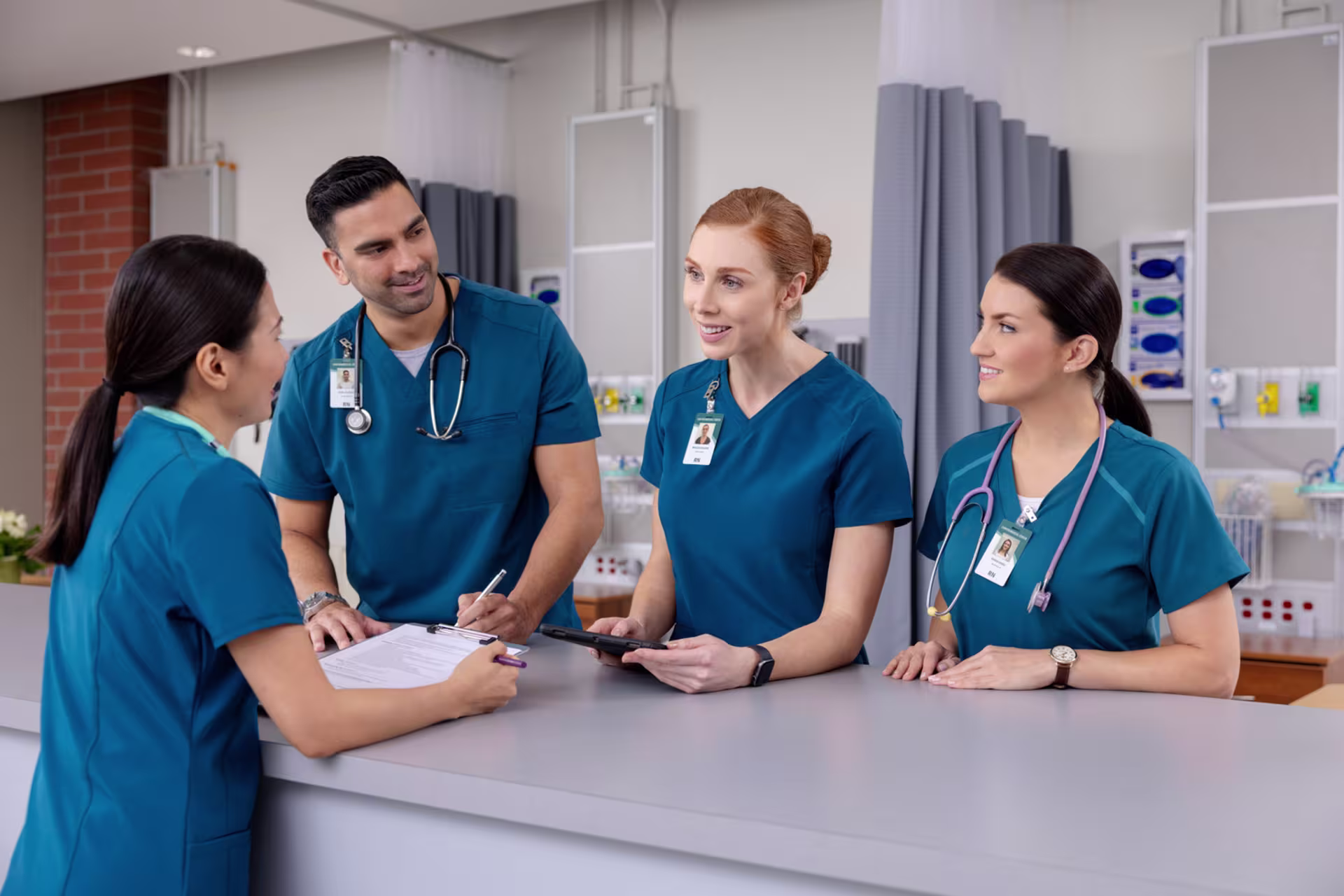 Nursing team in scrubs collaborating at nurses station, reviewing notes and discussing patient care in clinical setting.
