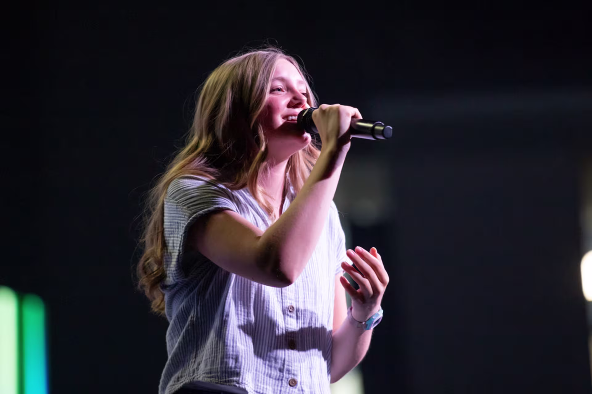 A female GCU student sings on stage with a microphone in a solo performance.