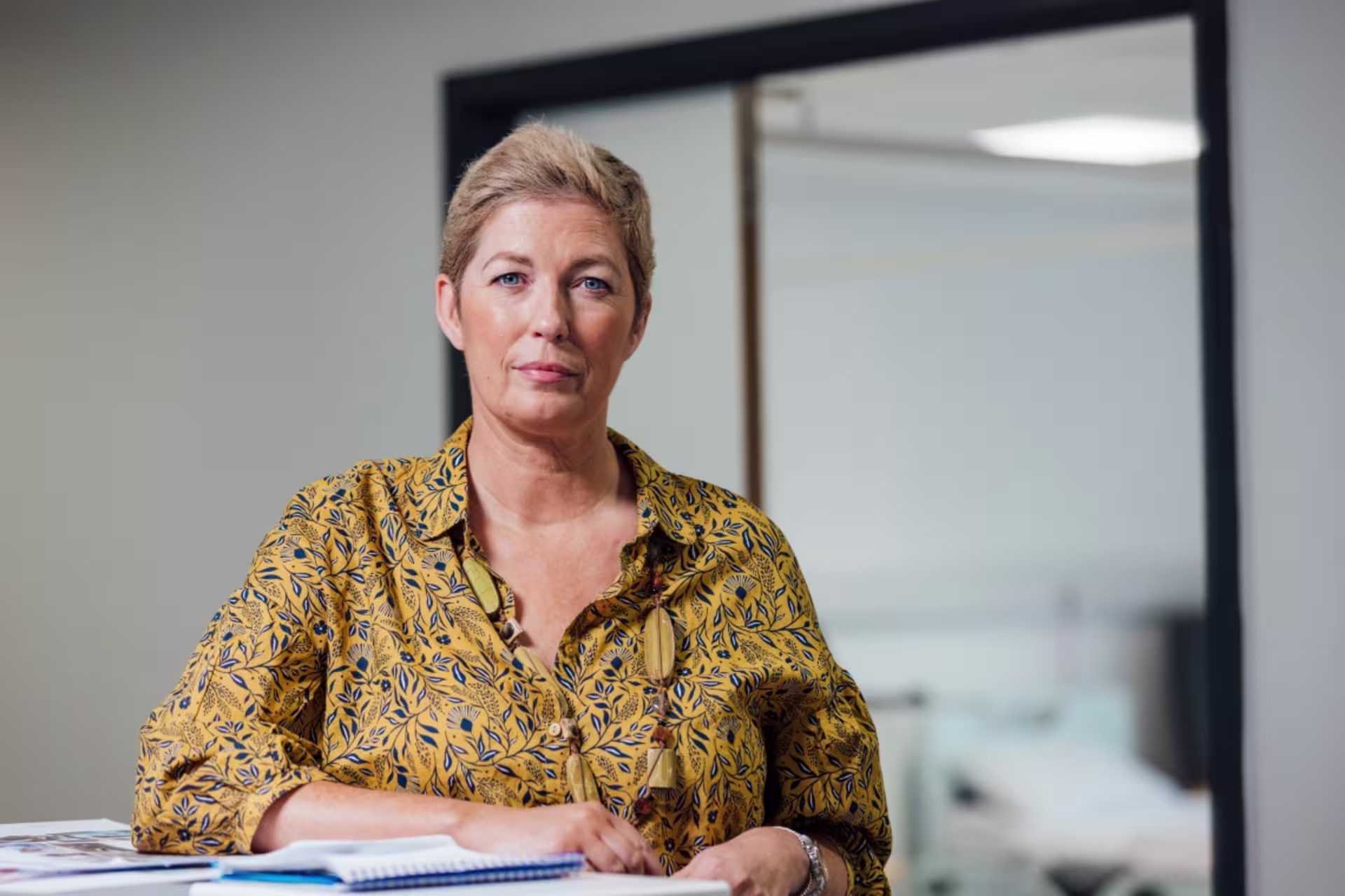 A female forensic psychologist sits at a desk with notes and papers in front of her in an office setting.