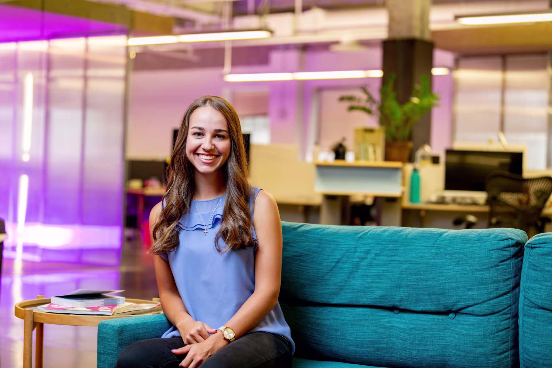 An international business student sits on a teal couch in a modern campus lounge with colorful lighting.