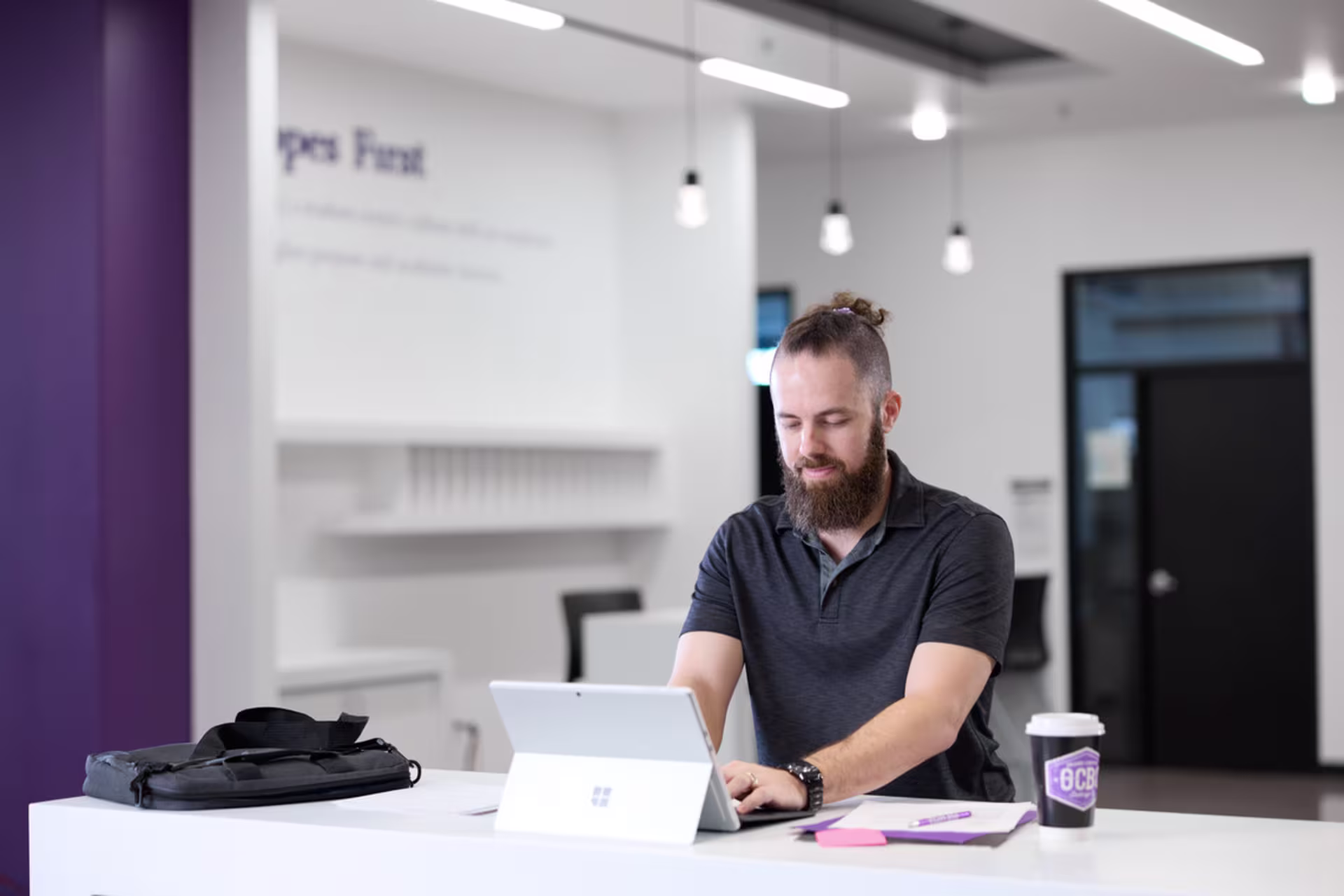 Male computer certificate student in a black shirt is typing on tablet in a modern office environment.