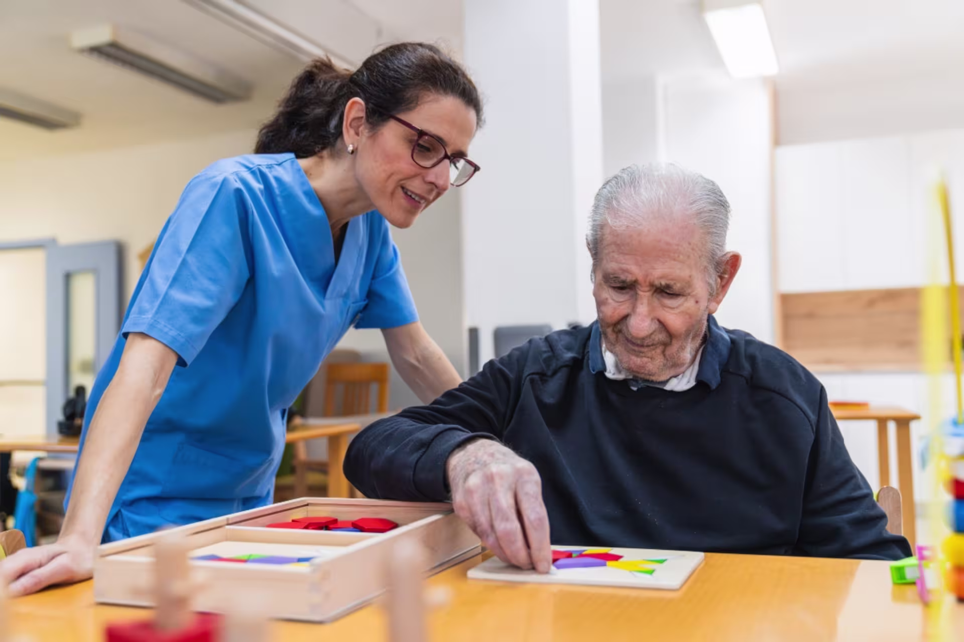An occupational therapist assists an older adult with a fine motor and cognitive therapy activity during a rehabilitation session.