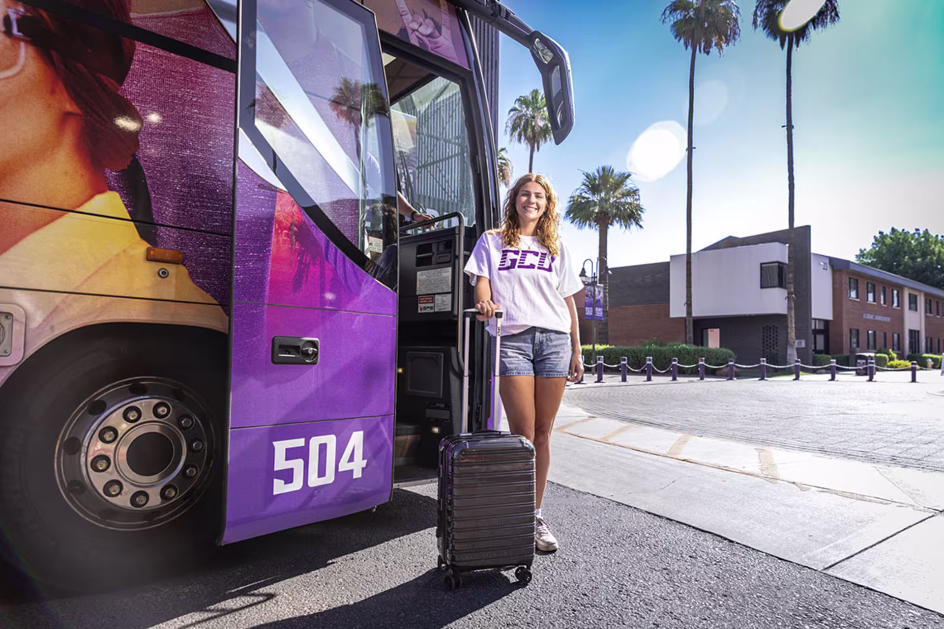 Student arriving on campus with luggage beside a GCU shuttle bus.