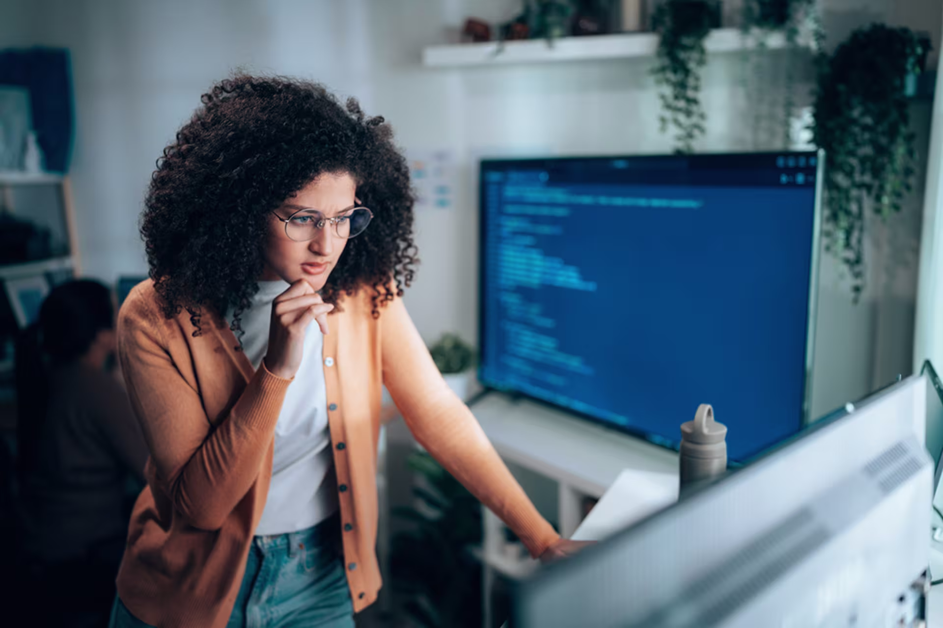 Cyber project professional student working at a computer, looking thoughtfully at a monitor displaying programming code.
