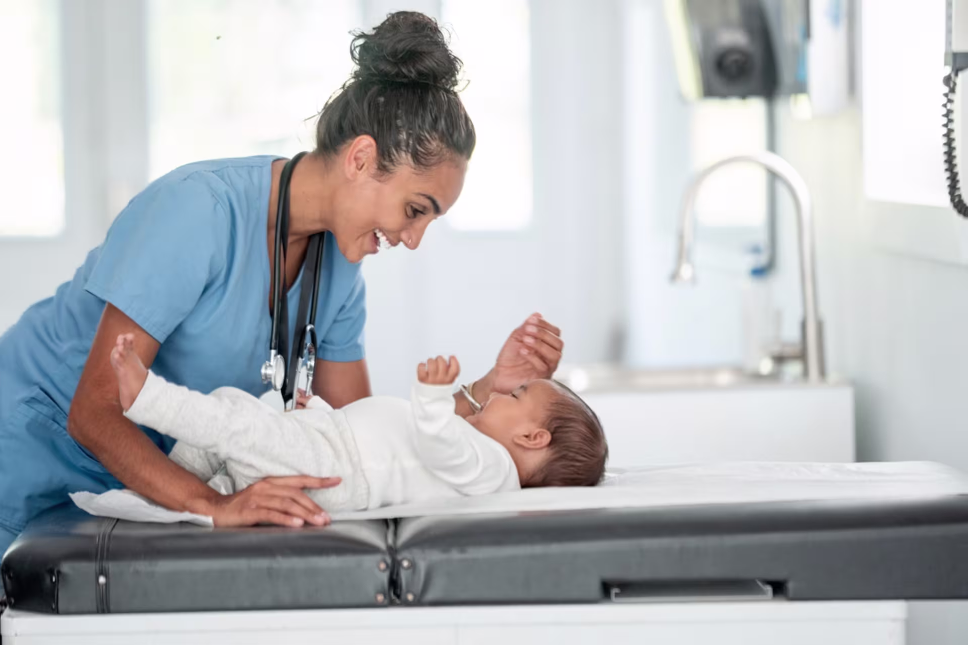 A female neonatal nurse smiles while examining an infant during a health assessment.