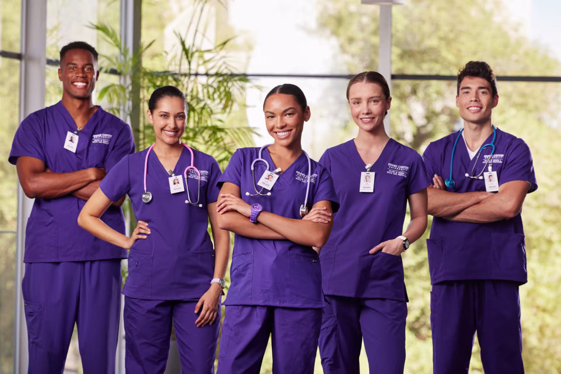 A group of male and female GCU nursing students pose while wearing purple scrubs and smiling.