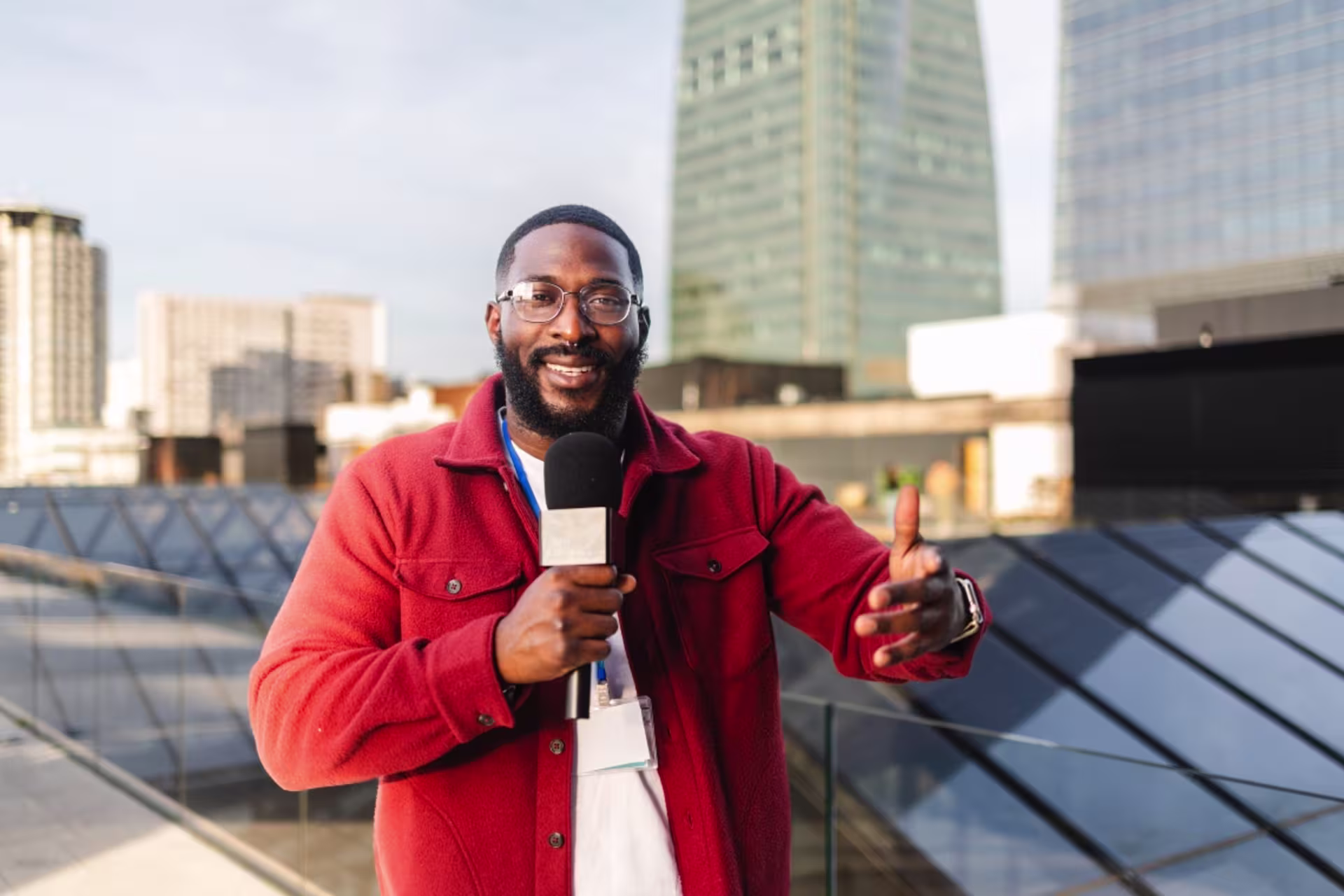 Male sports broadcaster reporting outdoors with a microphone and giving a thumbs-up.