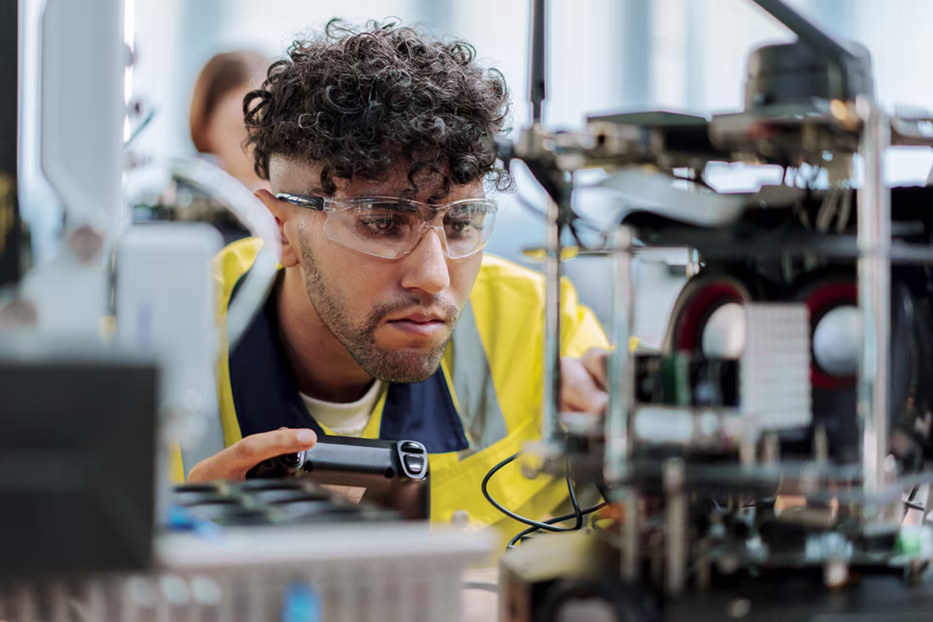Male undergraduate advanced manufacturing certificate student wearing safety glasses inspecting manufacturing equipment in a laboratory.