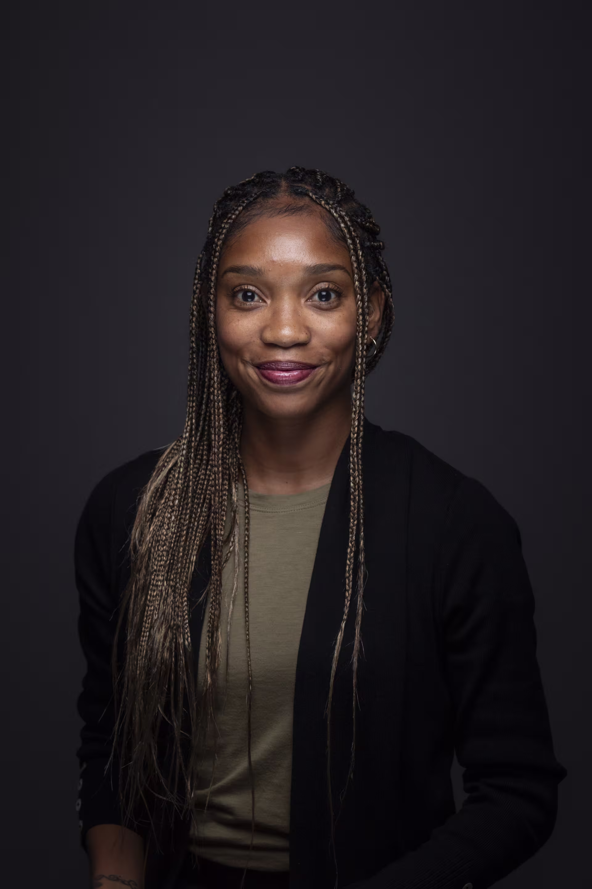 A studio-style headshot shows Dr. Desiree Jackson with long braided hair wearing a dark blazer over a neutral top, photographed against a dark background.