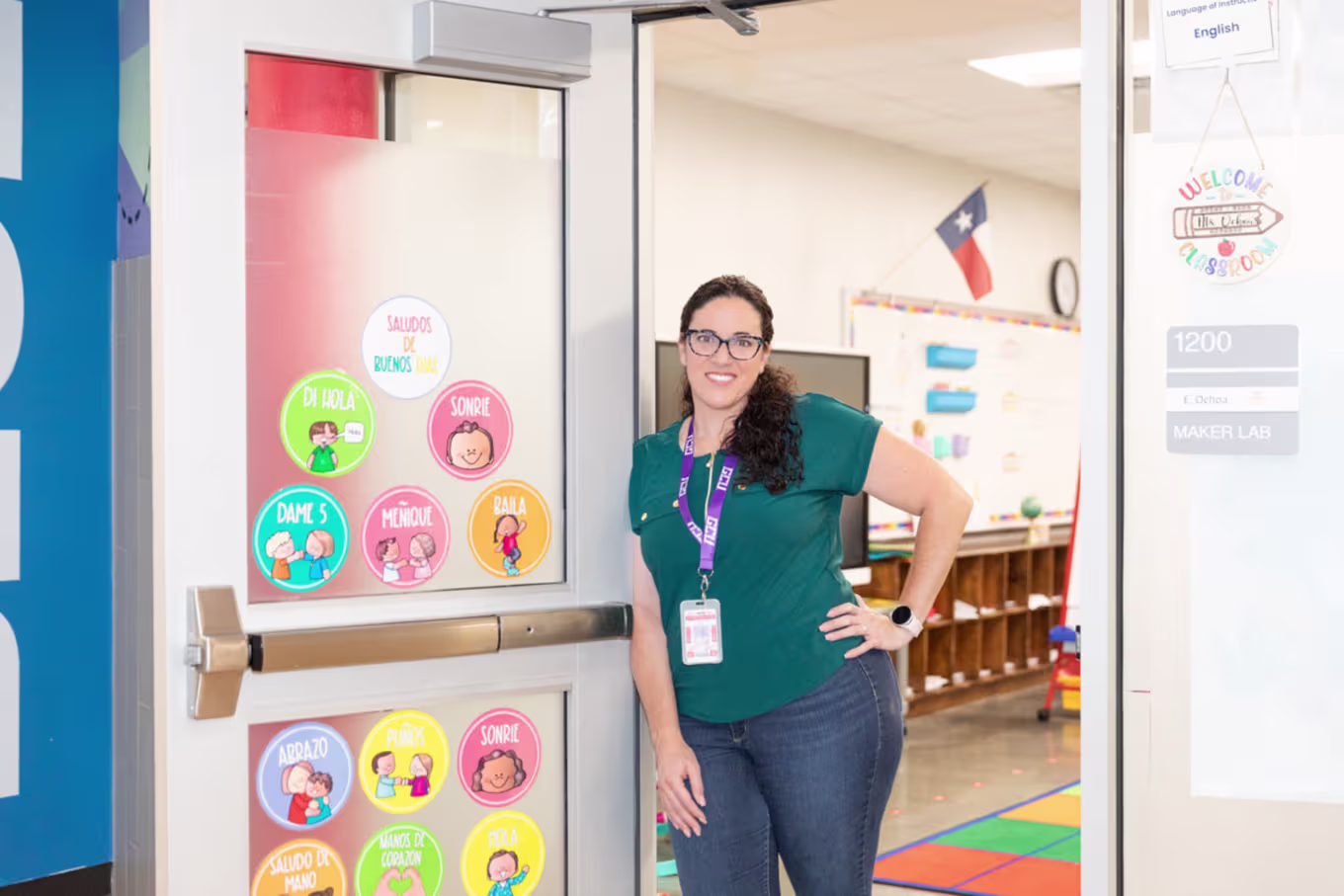 Female elementary teacher smiling and posing against their classroom door