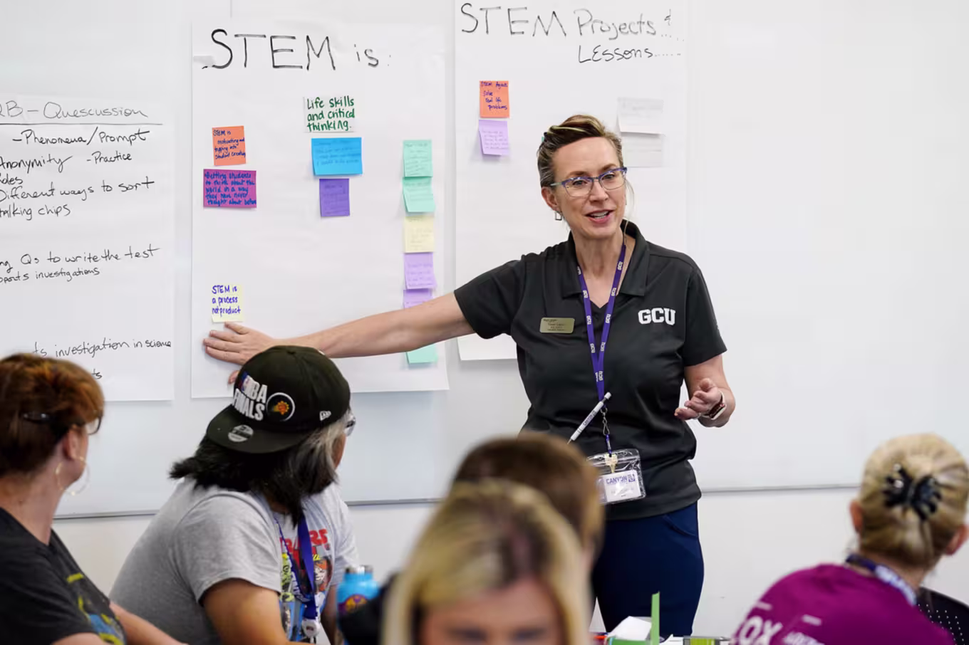 lady in black gcu shirt points to a stem lesson planning section of whiteboard in teacher training
