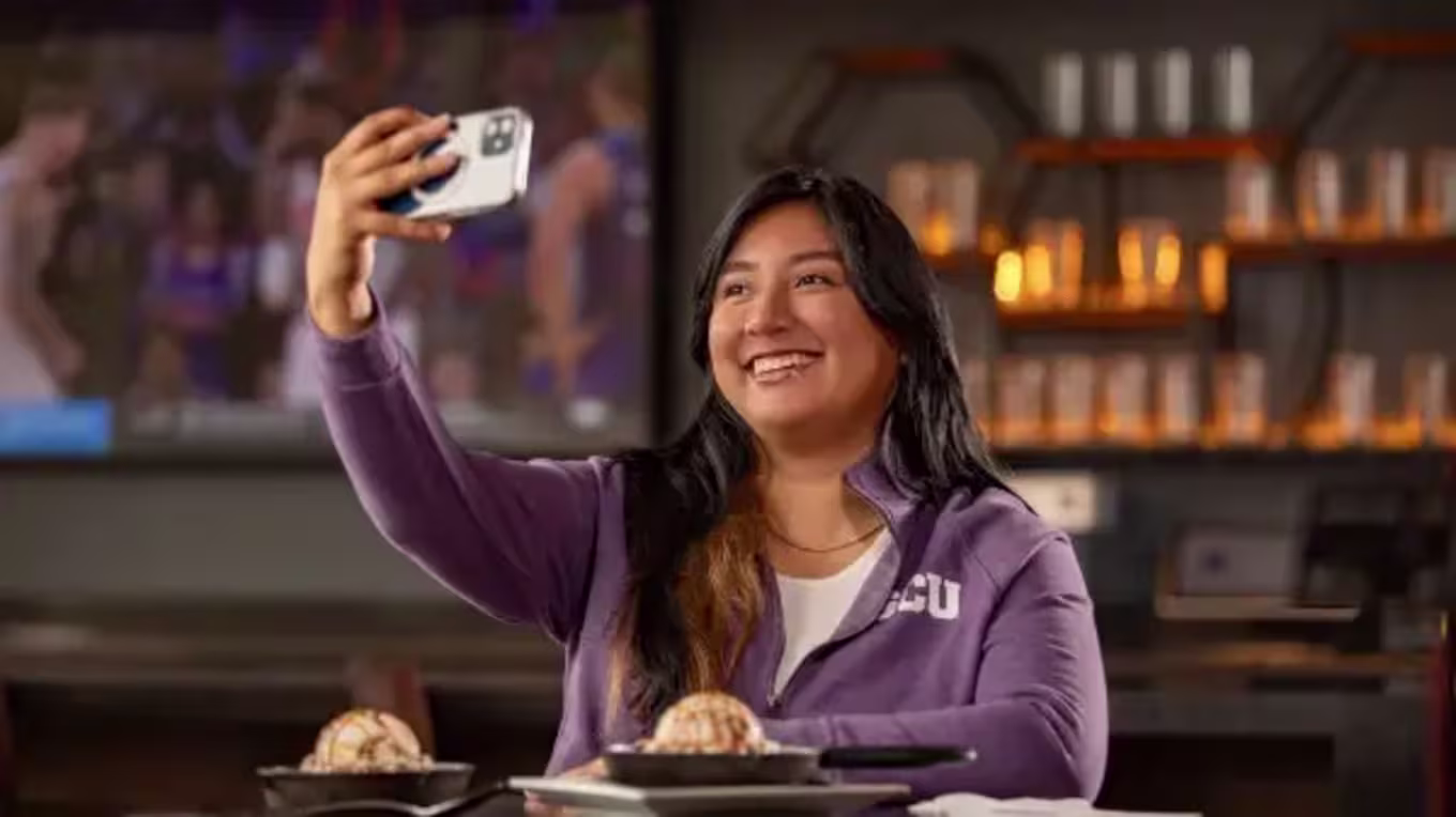 Student wearing GCU jacket sitting in restaurant taking a selfie
