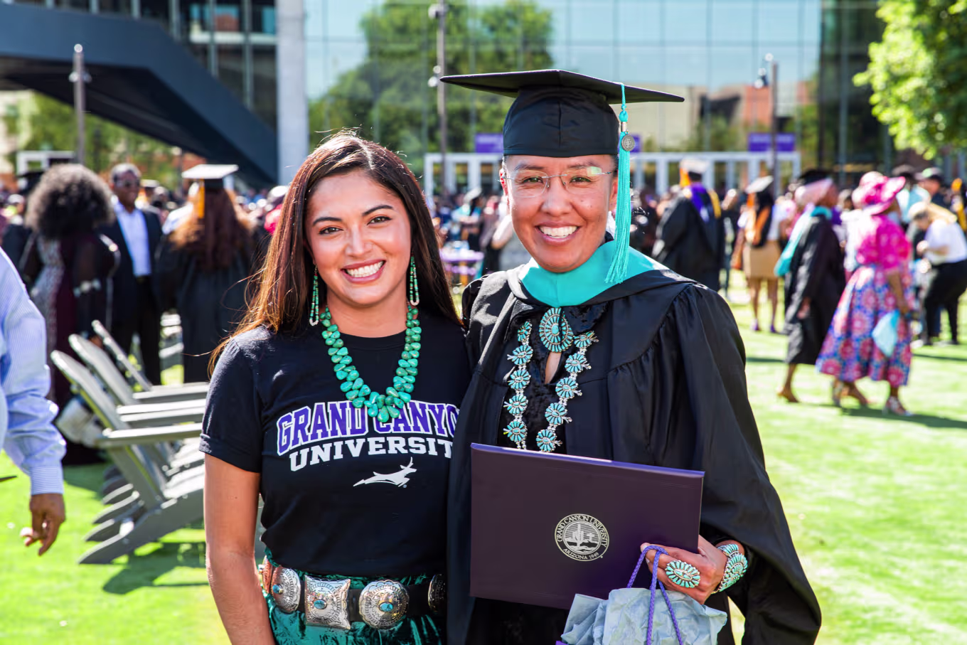 Female online MBA graduate smiling in cap and gown with daughter outside