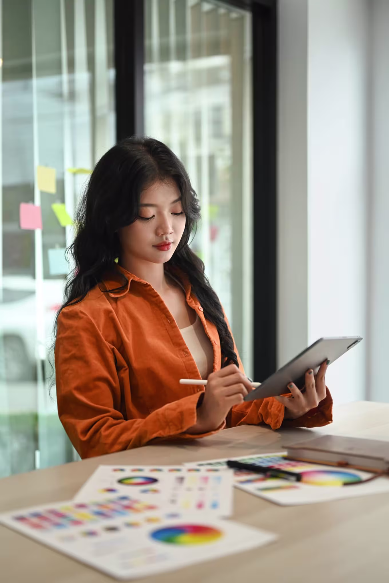 A female advertising and graphic design student working on tablet with color profiles on the table.