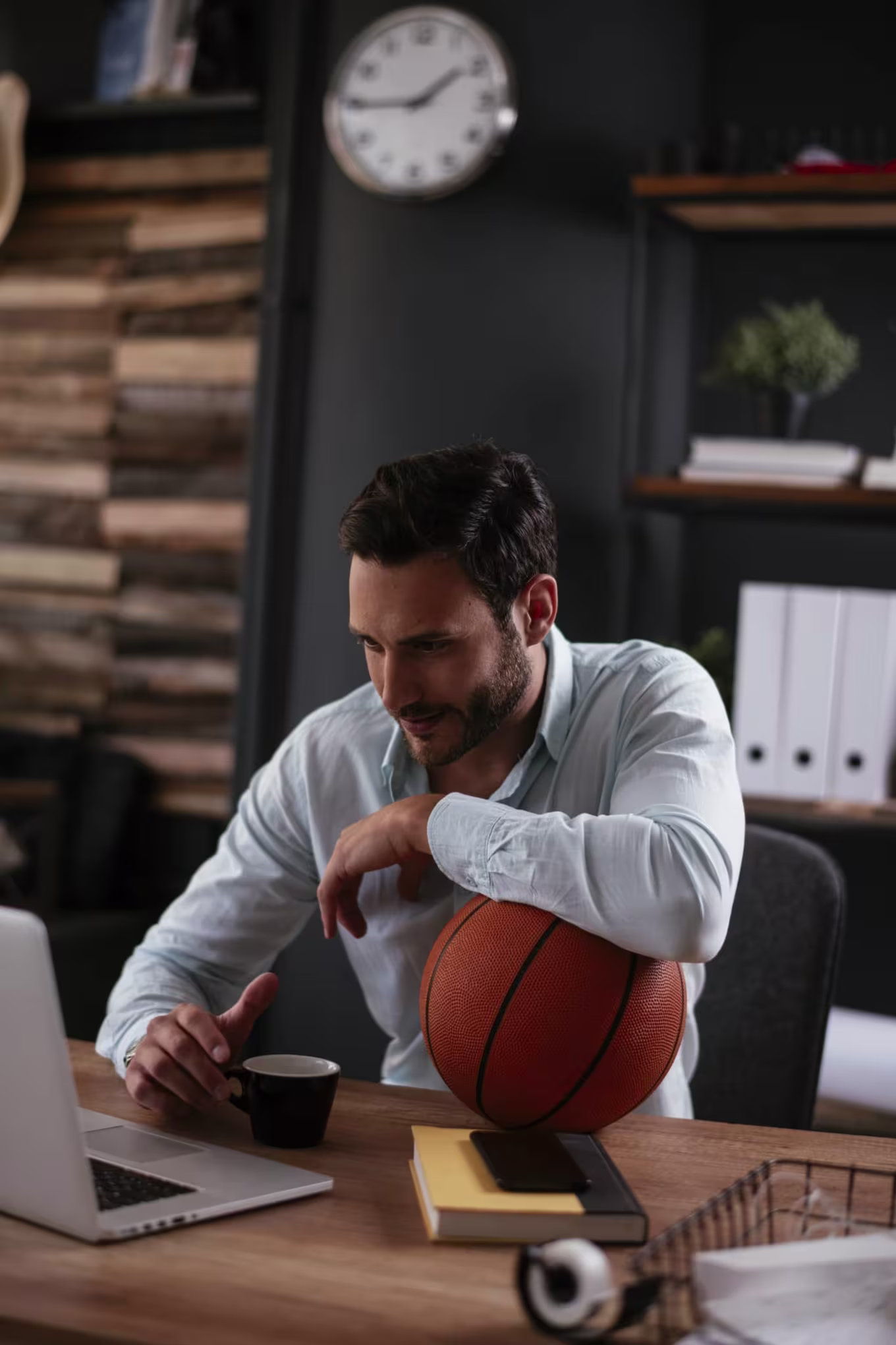A male sports business manager working in the office on a laptop.