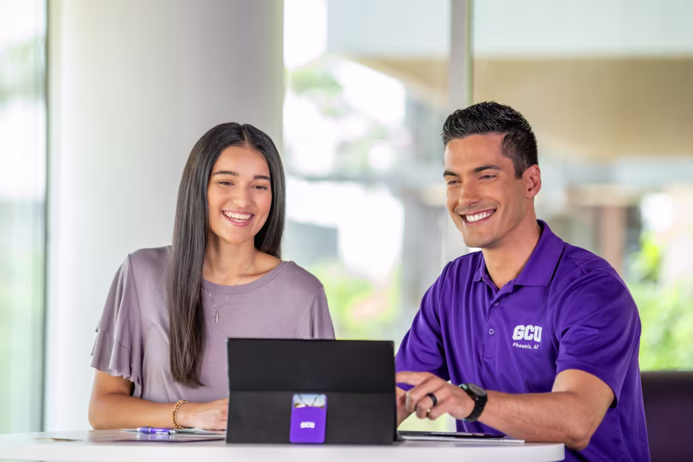 Brunette female with long hair smiles while male staff member from GCU career services in a purple branded polo points to a tablet.