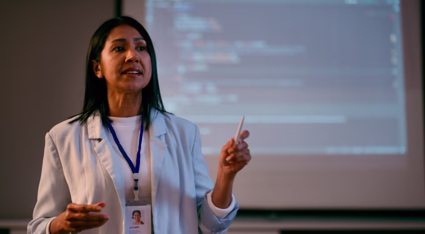 A person in a lab coat presents code on a screen, representing advanced study like a PhD or doctorate.