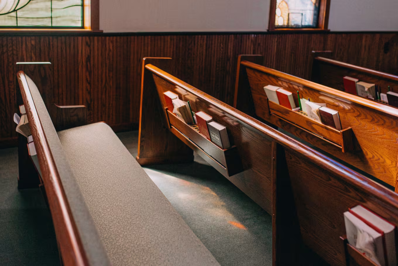 Church interior with wooden pews and hymnals, sunlight through stained glass windows — setting for various sermon styles and preaching traditions.