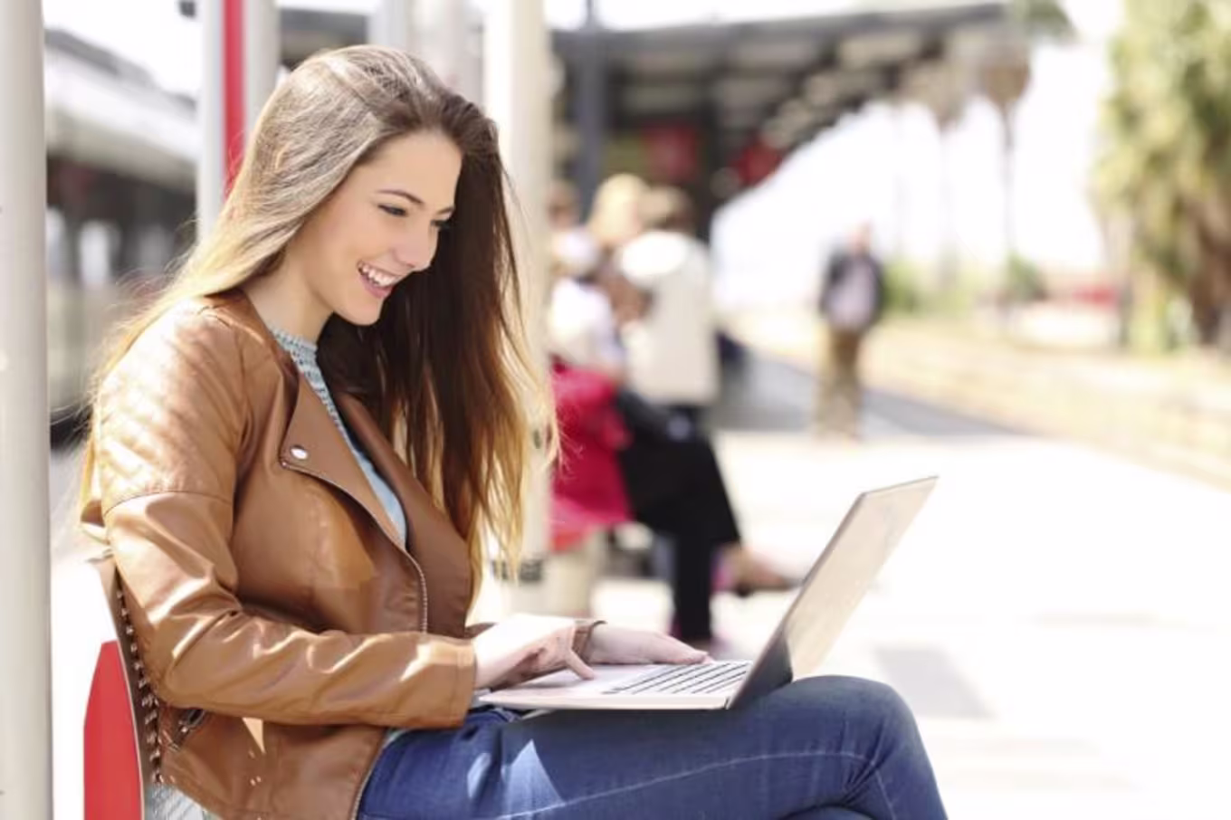 Young brunette woman smiles while using laptop at light rail station