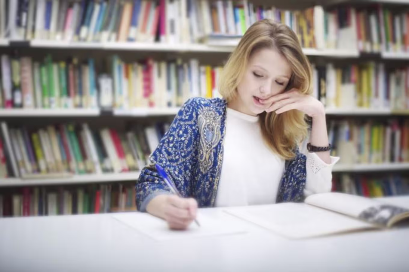 Blonde female student bites nails while studying in library