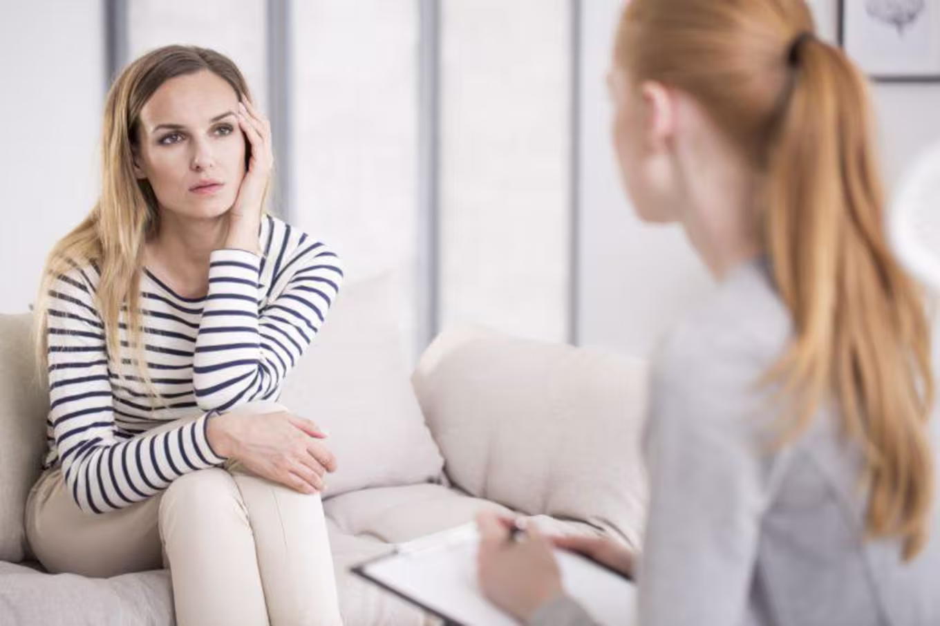 Young trauma counselor sits across beautiful woman in striped top