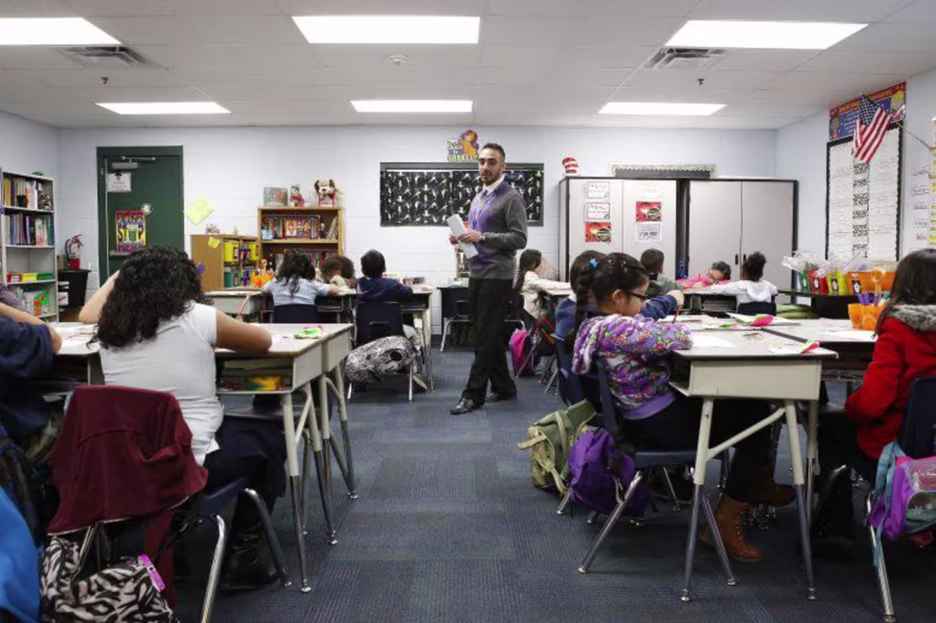 Hispanic male teacher paces classroom while students work
