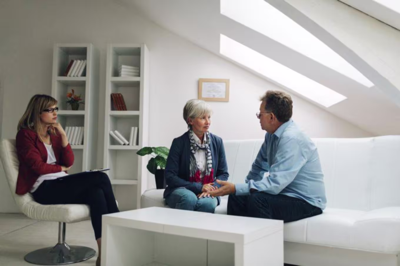 Female counselor observes older couple talking to each other face to face on white couch