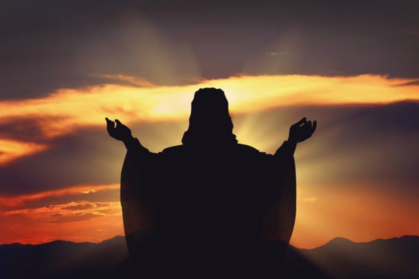 A silhouette of Jesus reaching towards the sunset
