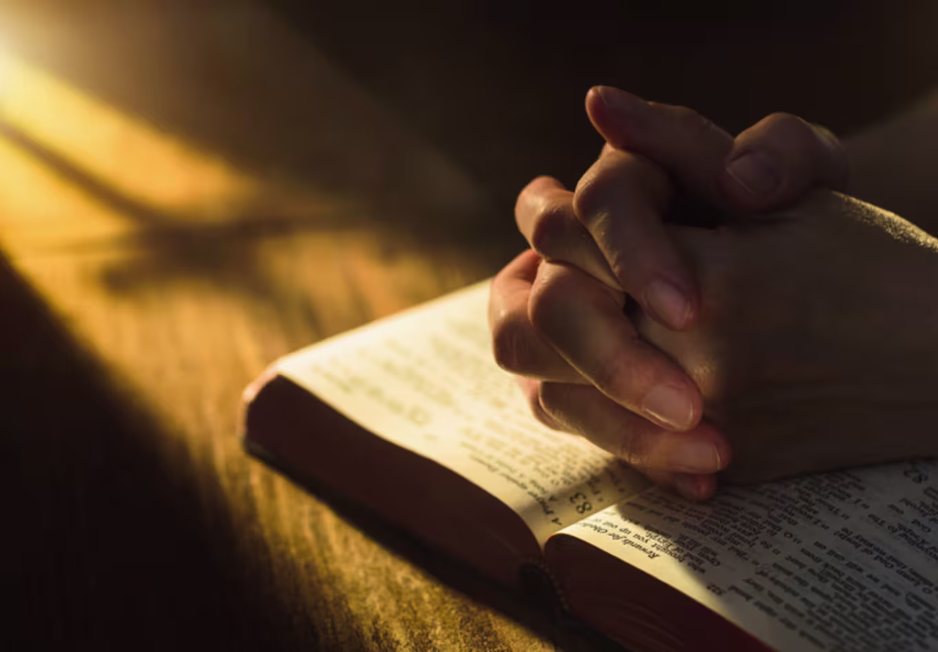 Close up of hands clasped on open Bible - stock photo