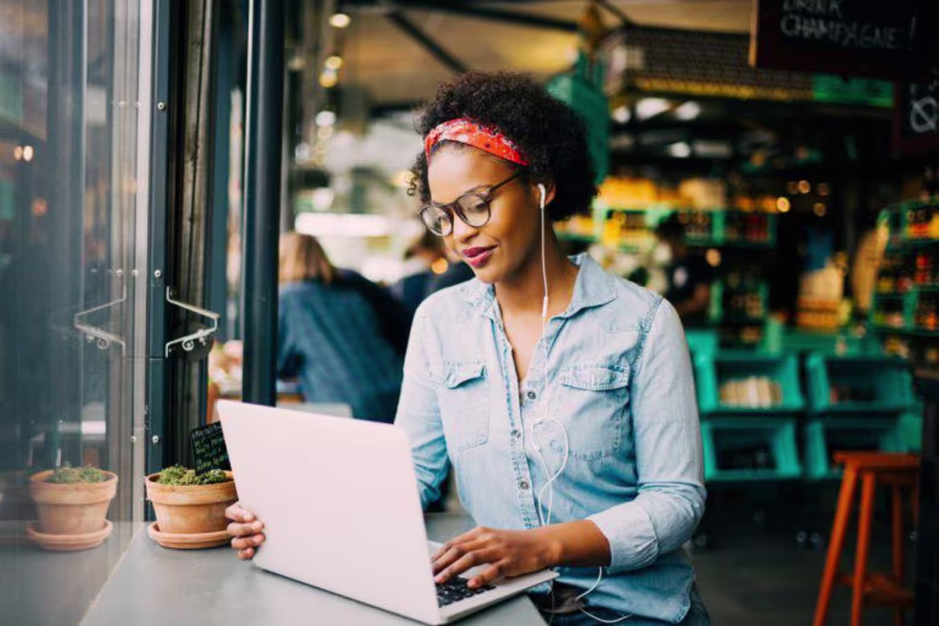 African-american women in a jean material long sleeved shirt with afro held up by red bandana uses laptop in a coffee shop