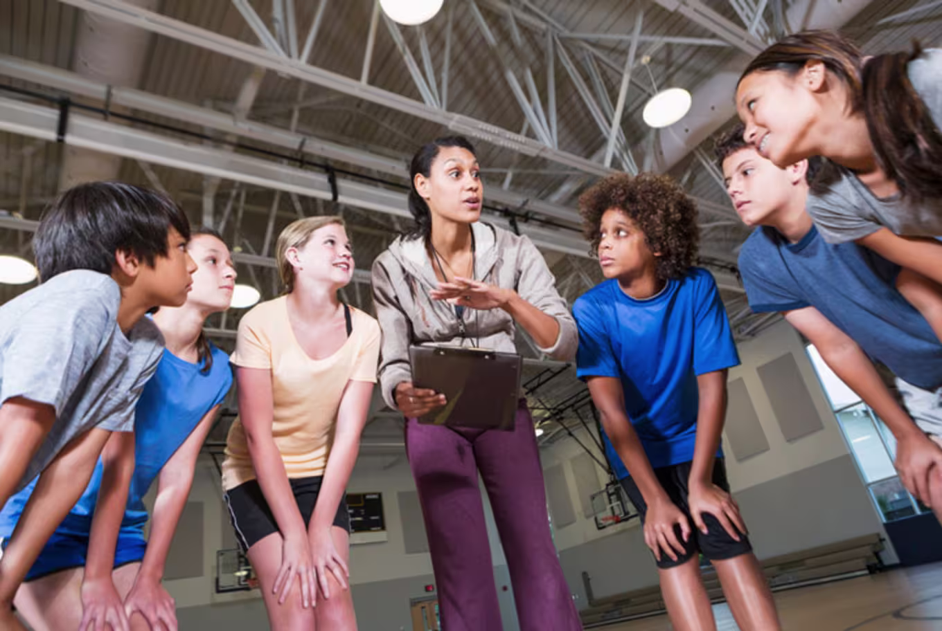 A PE teacher in a huddle with a group of her students