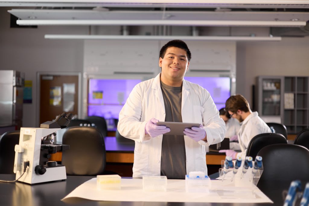Honors College male student in standing in science lab with coat on..