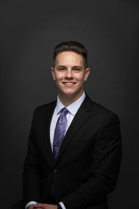 Jesse Traut headshot wearing black jacket and purple tie.