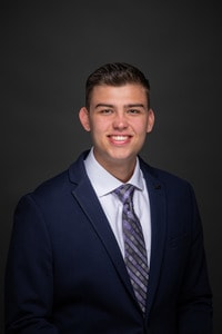 Matthew Kerin headshot in suit and purple striped tie.