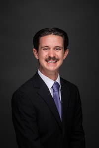 Steven Owens headshot in suit and purple tie.