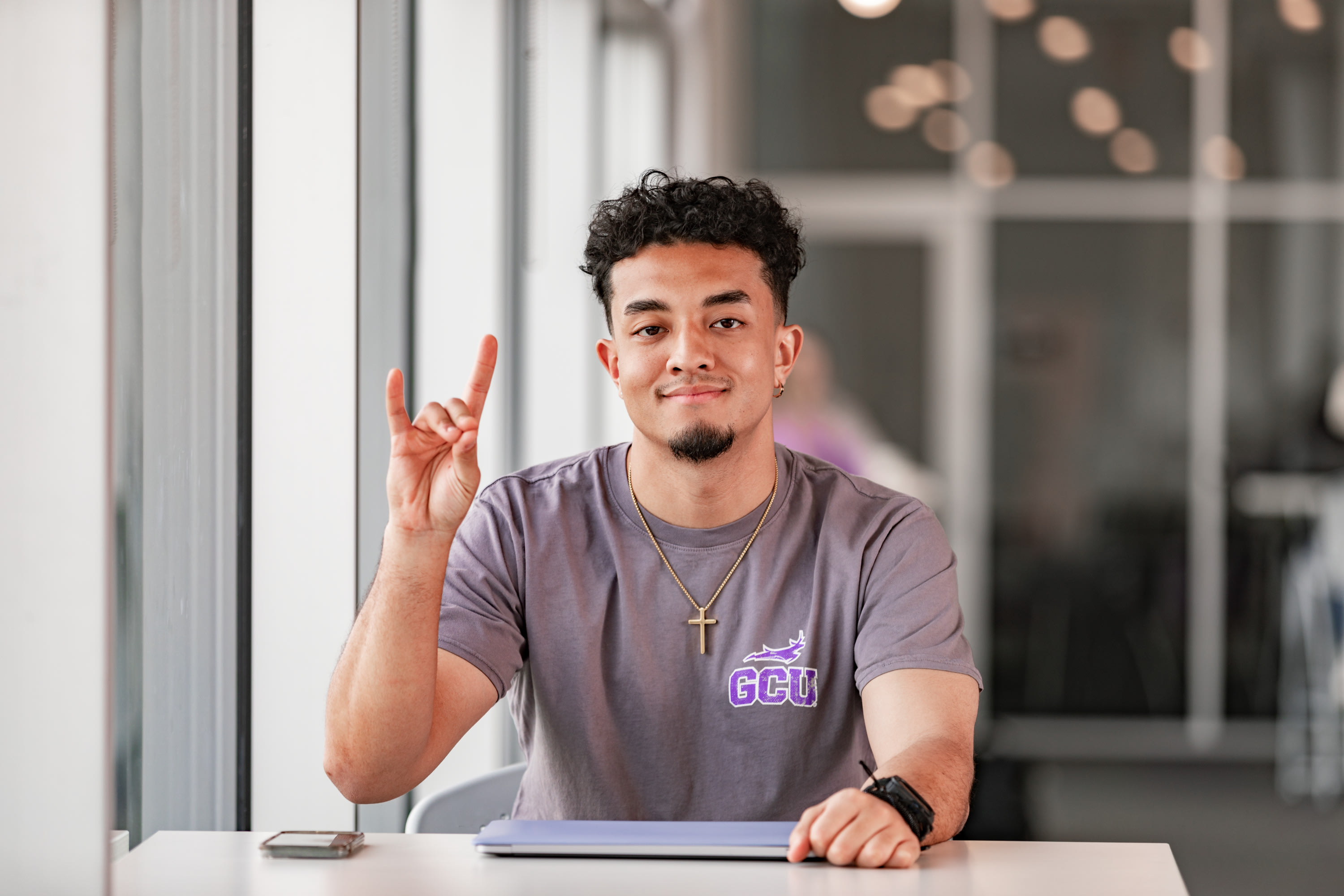 Student holding lopes up sitting at a table with computer