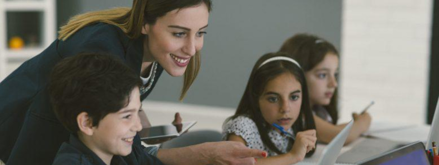 Female teacher helping young children navigate technology