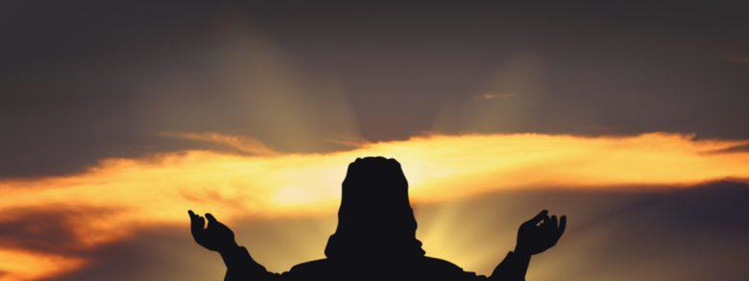 A silhouette of Jesus reaching towards the sunset