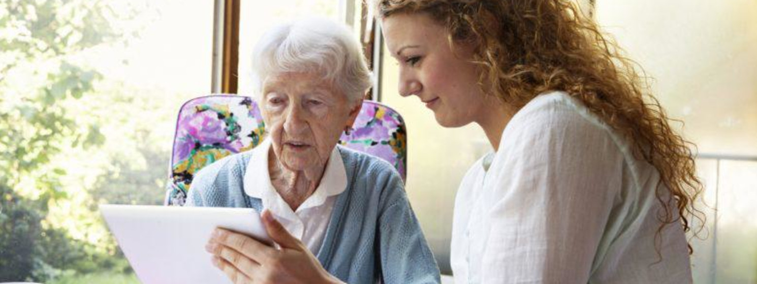 Woman with long curly hair shows elderly woman something on tablet